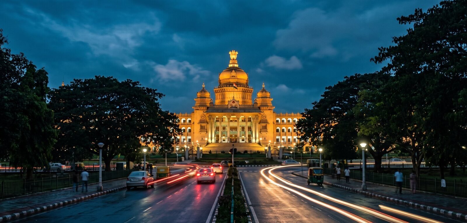 Vidhana Soudha in Bengaluru lit up at dusk, with traffic trails on the road in front