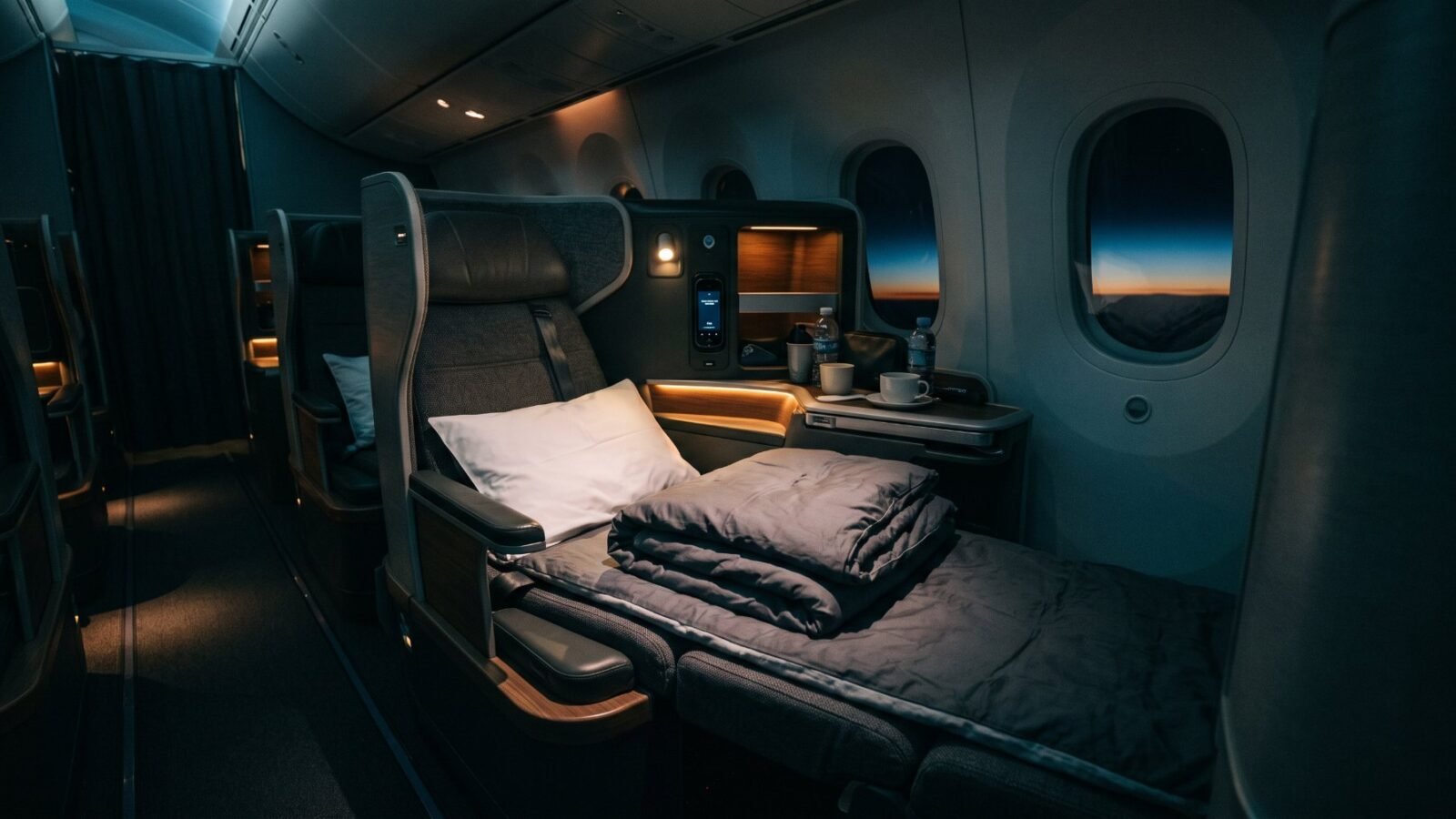 A lie-flat business class seat made up as a bed, with a window showing dusk outside