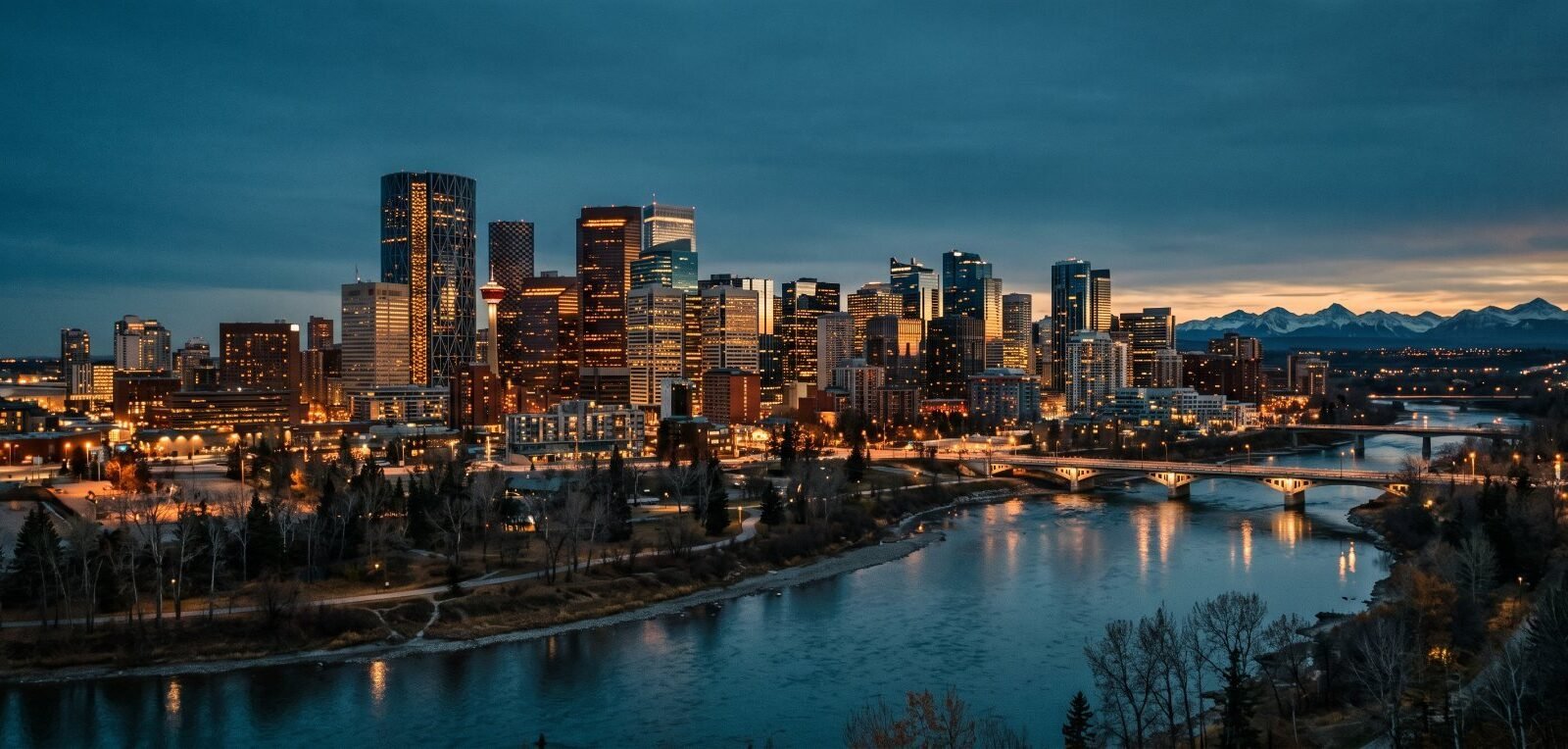 Downtown Calgary at dusk above the Bow River, the Rockies on the horizon